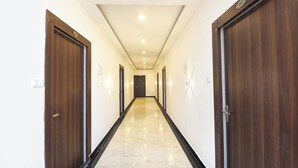 A hallway with wooden doors, marble flooring, and recessed ceiling lighting. - Fabhotel Haritaj (Varanasi)