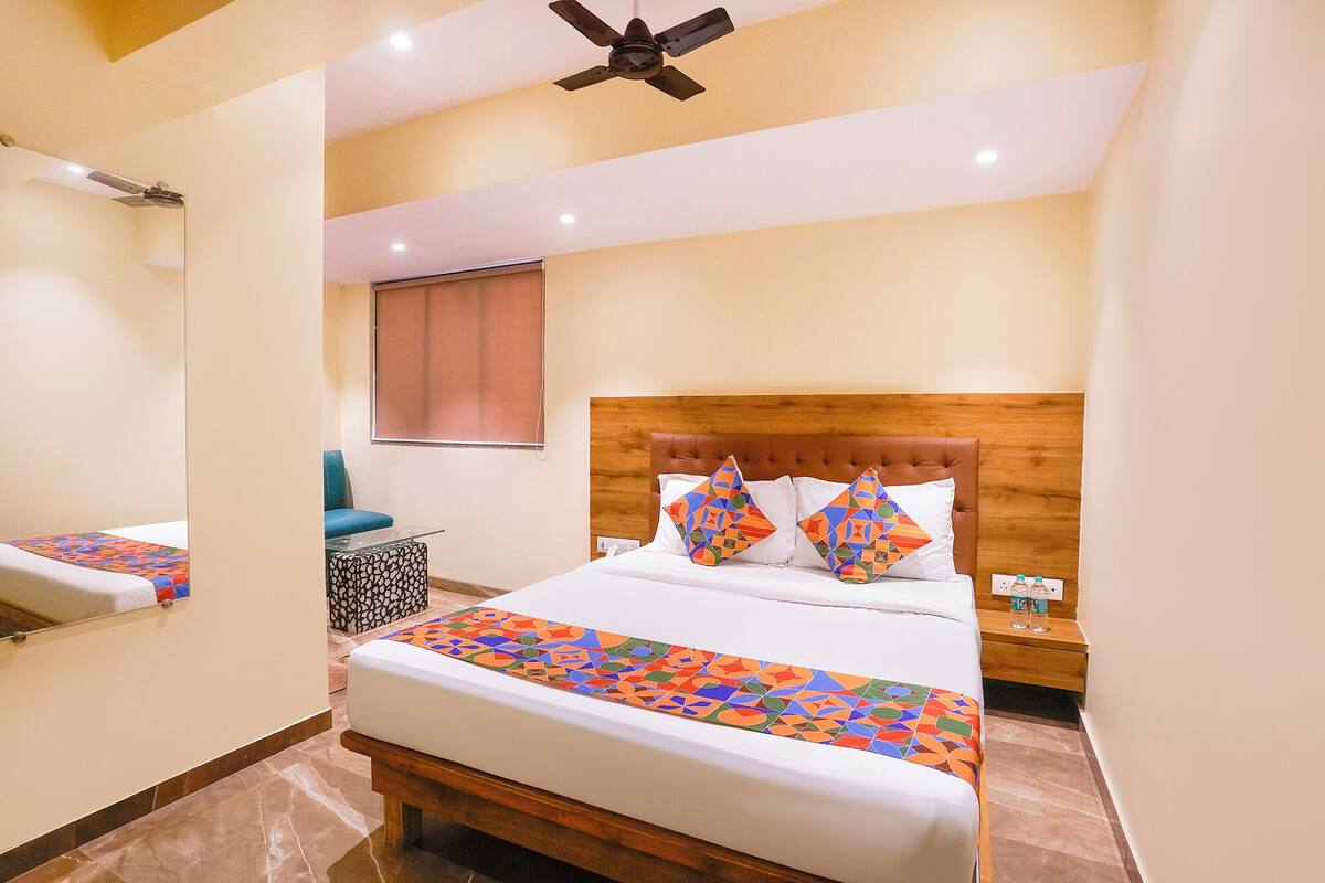 A hotel room with a bed, a wooden headboard, a nightstand, a chair, a window, and a ceiling fan.
