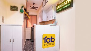 A hotel reception area with a 'fab hotels' sign, a 'SAMRATH LODGING & BOARDING' sign, a ceiling fan, and a small shrine with marigold flowers. - Fabhotel Samrath (Mumbai)