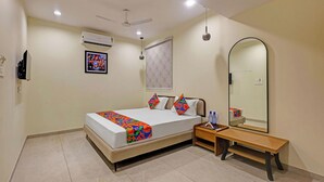 A bedroom with a bed, bedside table, mirror, and ceiling fan. - Fabhotel Elixir Inn (Surat)