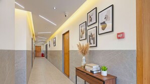 A modern hallway with a wooden desk, framed artwork, and a fire extinguisher. - Fabhotel Elixir Inn (Surat)