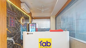 A reception area with a marble wall, a reception desk labeled 'fab hotels', and a window with blinds. - Fabhotel Elixir Inn (Surat)