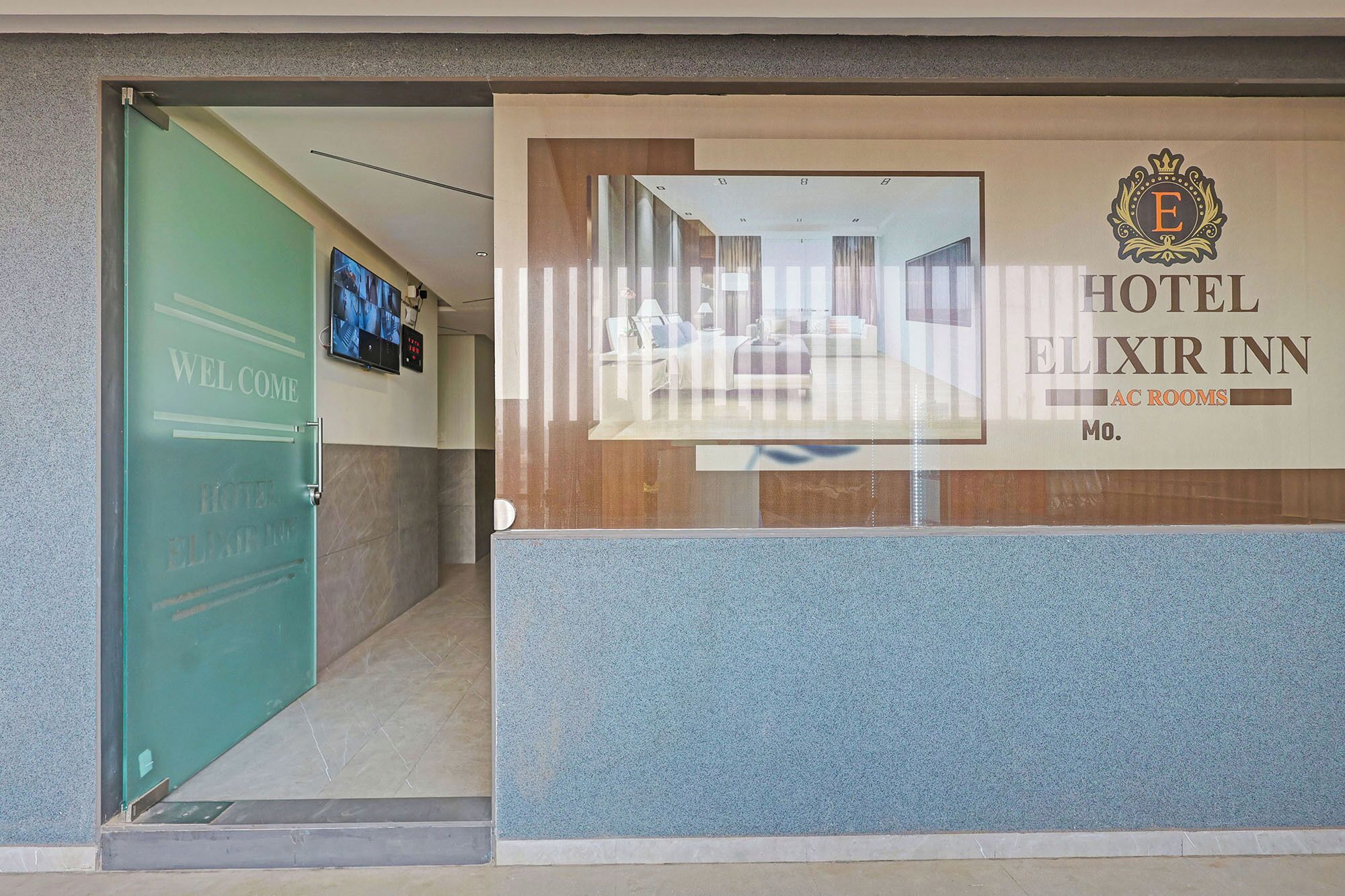 A hotel entrance with a reception desk, a green door, and a window displaying a room interior.