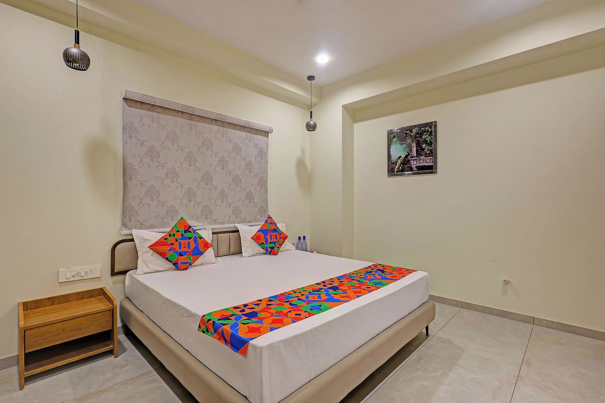 A bedroom with a bed, a nightstand, a window with curtains, a wall-mounted picture, and a ceiling light.