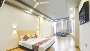 Quarto de hotel com uma cama grande, uma escrivaninha, uma cadeira, um ventilador de teto e uma televisão na parede.