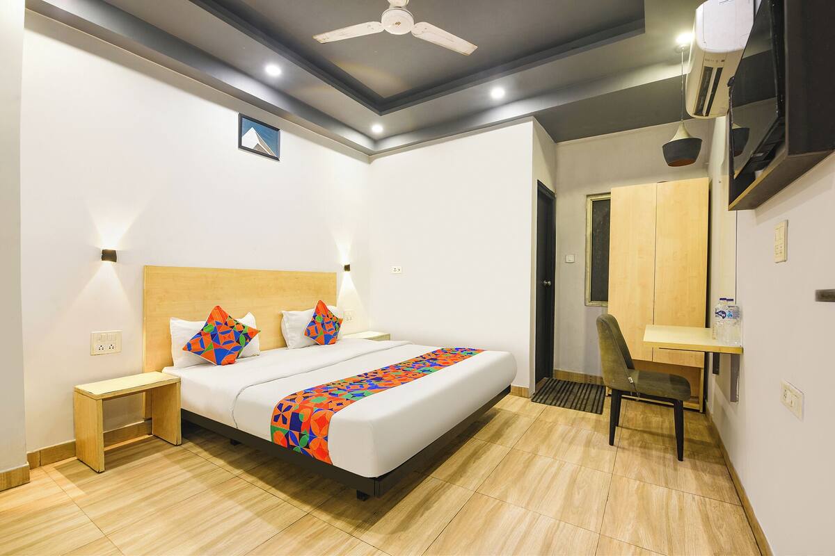 A hotel room with a bed, bedside table, chair, desk, and a ceiling fan.