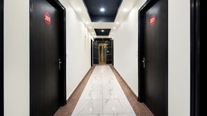 Corredor moderno de hotel, com portas pretas identificadas por números de quarto, piso de mármore e iluminação embutida no teto.
