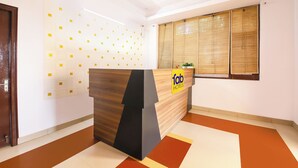 A hotel reception area with a wooden reception desk, a wall-mounted security camera, and a window with blinds. - Fabhotel 9 Palm (Dehradun)
