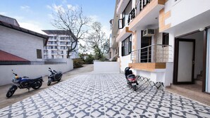 A courtyard with patterned tiles, two parked scooters, and a building with balconies and a door. - Fabhotel 9 Palm (Dehradun)