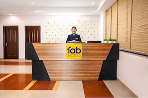 A reception desk with a logo for 'fab hotels,' a receptionist, and a patterned wall behind. - Fabhotel 9 Palm (Dehradun)