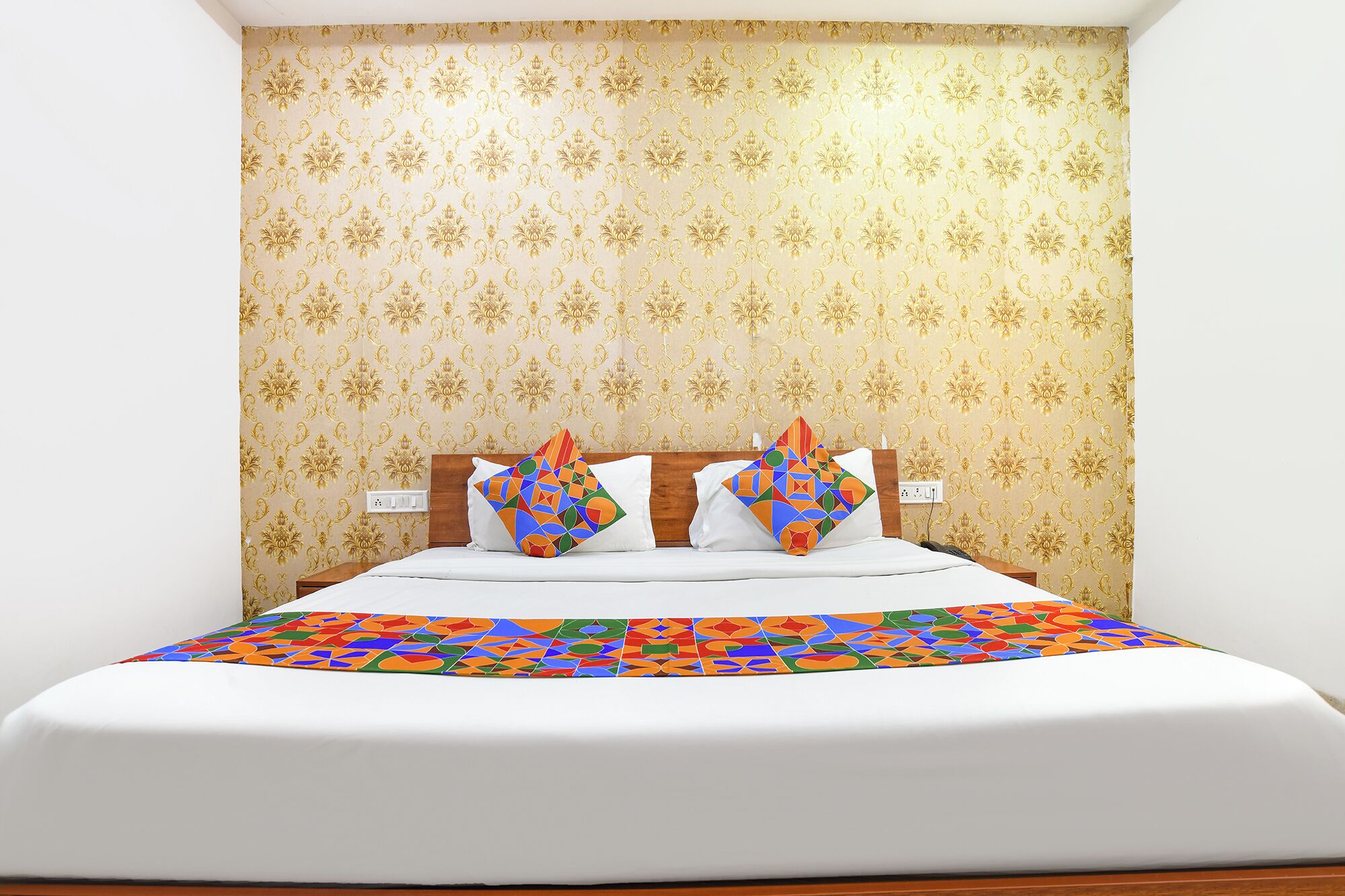 Una camera d'albergo con un letto, due cuscini con motivi geometrici e una carta da parati decorata.