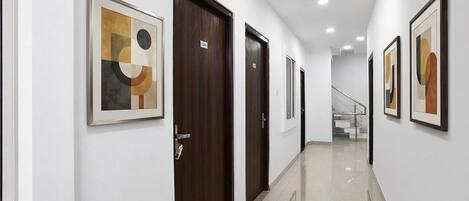 A hallway with framed abstract art, wooden doors, and a staircase in the background.
