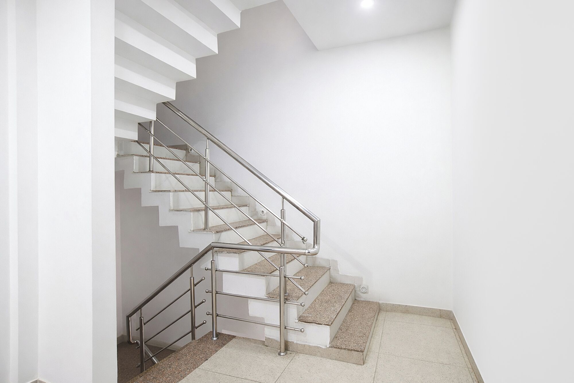 Un escalier moderne avec une rampe en métal, des murs blancs et un sol carrelé.