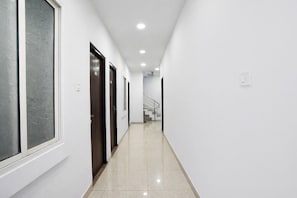 A narrow, well-lit hallway with white walls and a tiled floor, leading to a staircase. - Fabhotel Shivay (Indore)