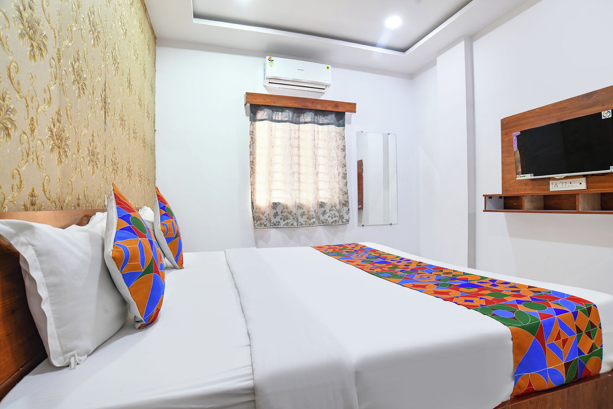 Una camera d'albergo con un letto, una TV a muro e una finestra con tende.