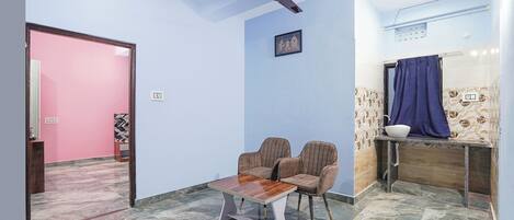Una habitación con ventilador de techo, una pequeña mesa con dos sillas, un lavamanos con cortina azul y papel tapiz estampado.