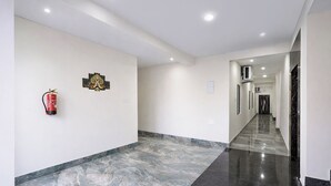 A hallway with a fire extinguisher mounted on the wall, a decorative wall piece, and a marble floor. - Fabhotel Golden Suites Near Puri Beach (Puri)