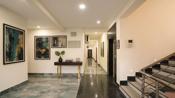 A hallway with marble flooring, a console table with decorative items, framed artwork on the walls, and a staircase with metal railings. - Fabhotel Golden Suites Near Puri Beach (Puri)