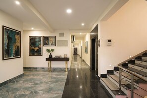 A hallway with marble flooring, a console table with decorative items, framed artwork on the walls, and a staircase with metal railings. - Fabhotel Golden Suites Near Puri Beach (Puri)