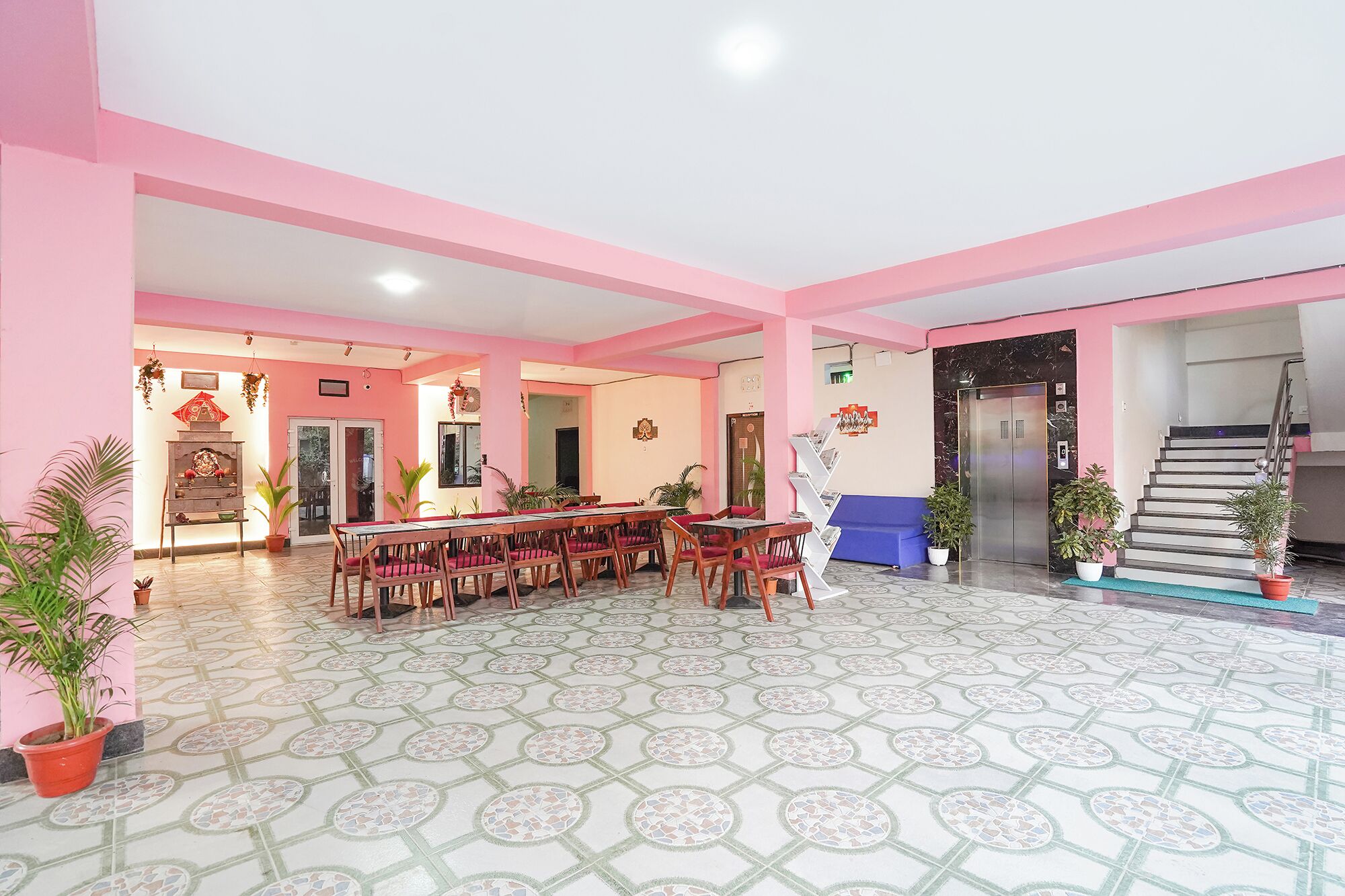A spacious lobby with a long dining table and chairs, a reception desk, and a staircase leading to an elevator.