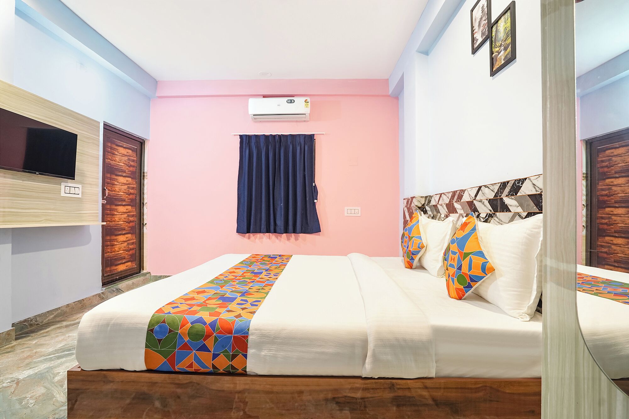 A hotel room with a bed, a TV, an air conditioner, and a window with curtains.
