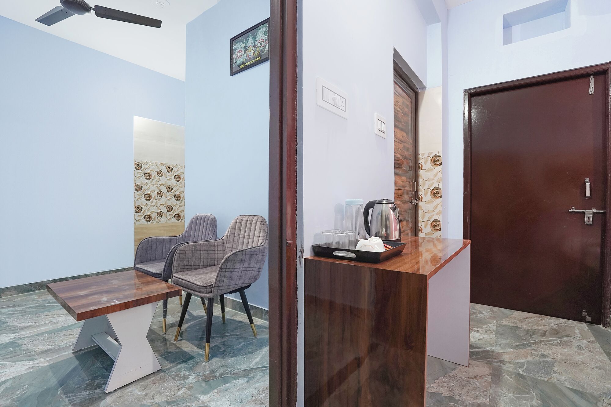 A room with a wooden desk, two chairs, a ceiling fan, and a door.