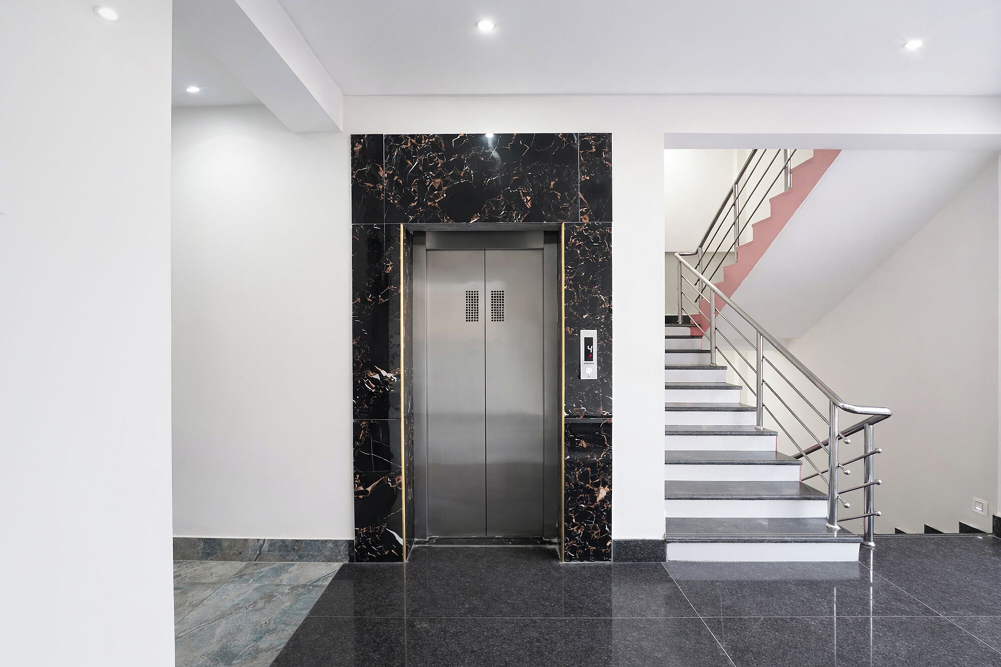 Um elevador moderno com acabamento em mármore, uma escadaria com guarda-corpos de metal e um design de interiores limpo e minimalista.