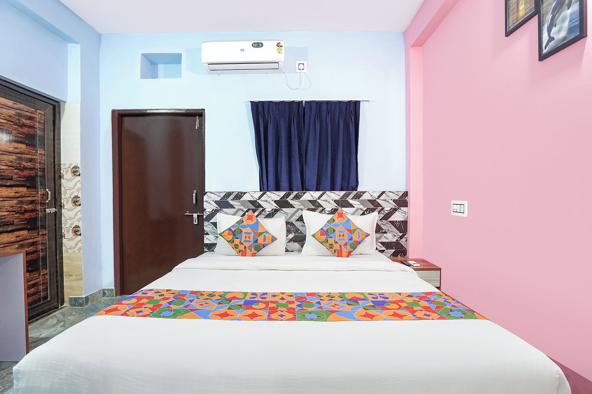 Habitación de hotel con cama, mesita de noche, aire acondicionado de pared, puerta y ventana con cortinas.