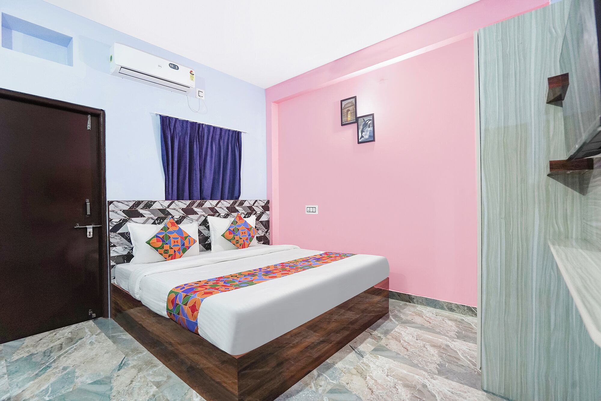A bedroom with a bed, a door, a wall-mounted air conditioner, and a pink wall.