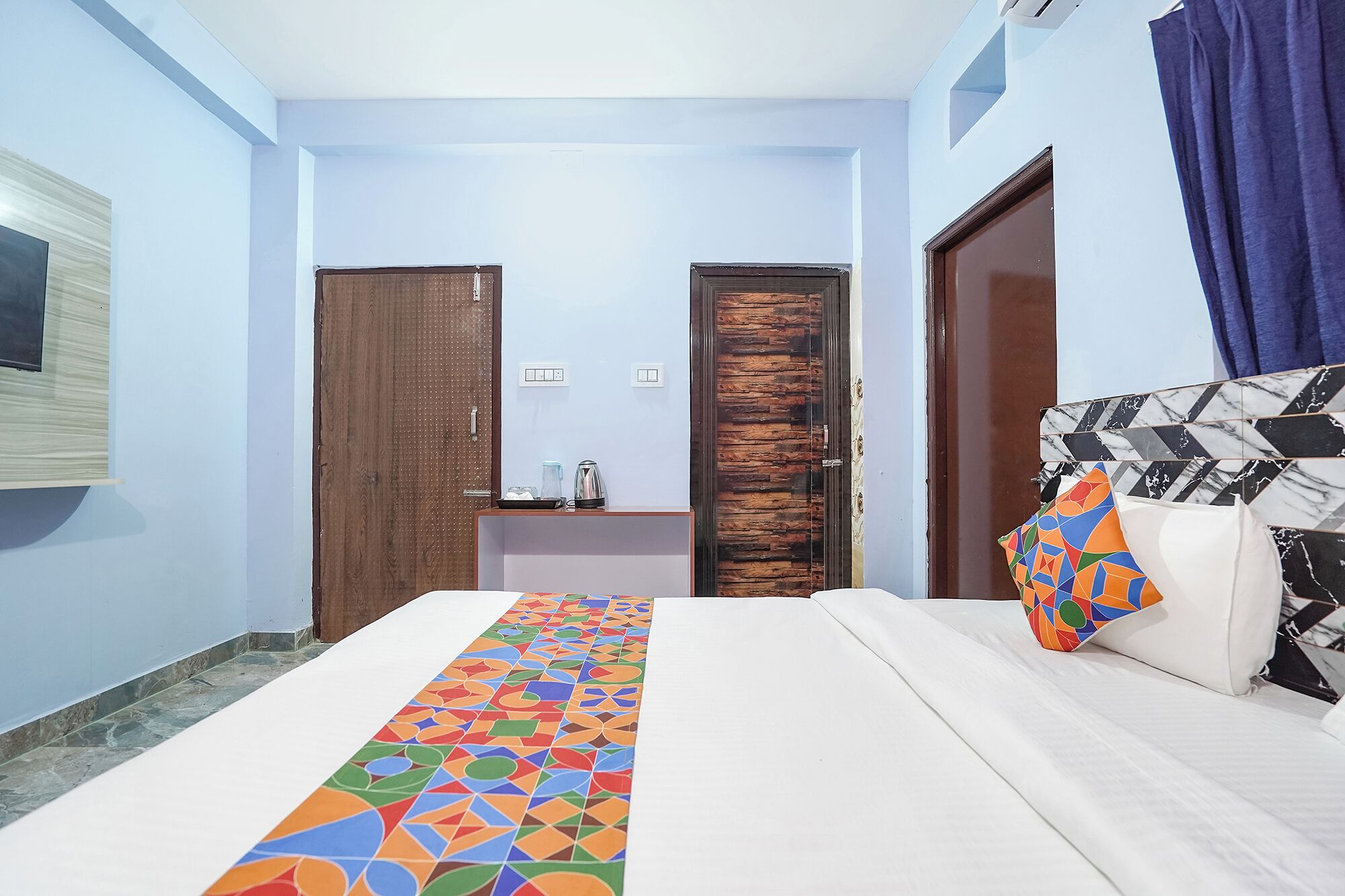 A hotel room with a bed, a bedside table, a mirror, and a door.