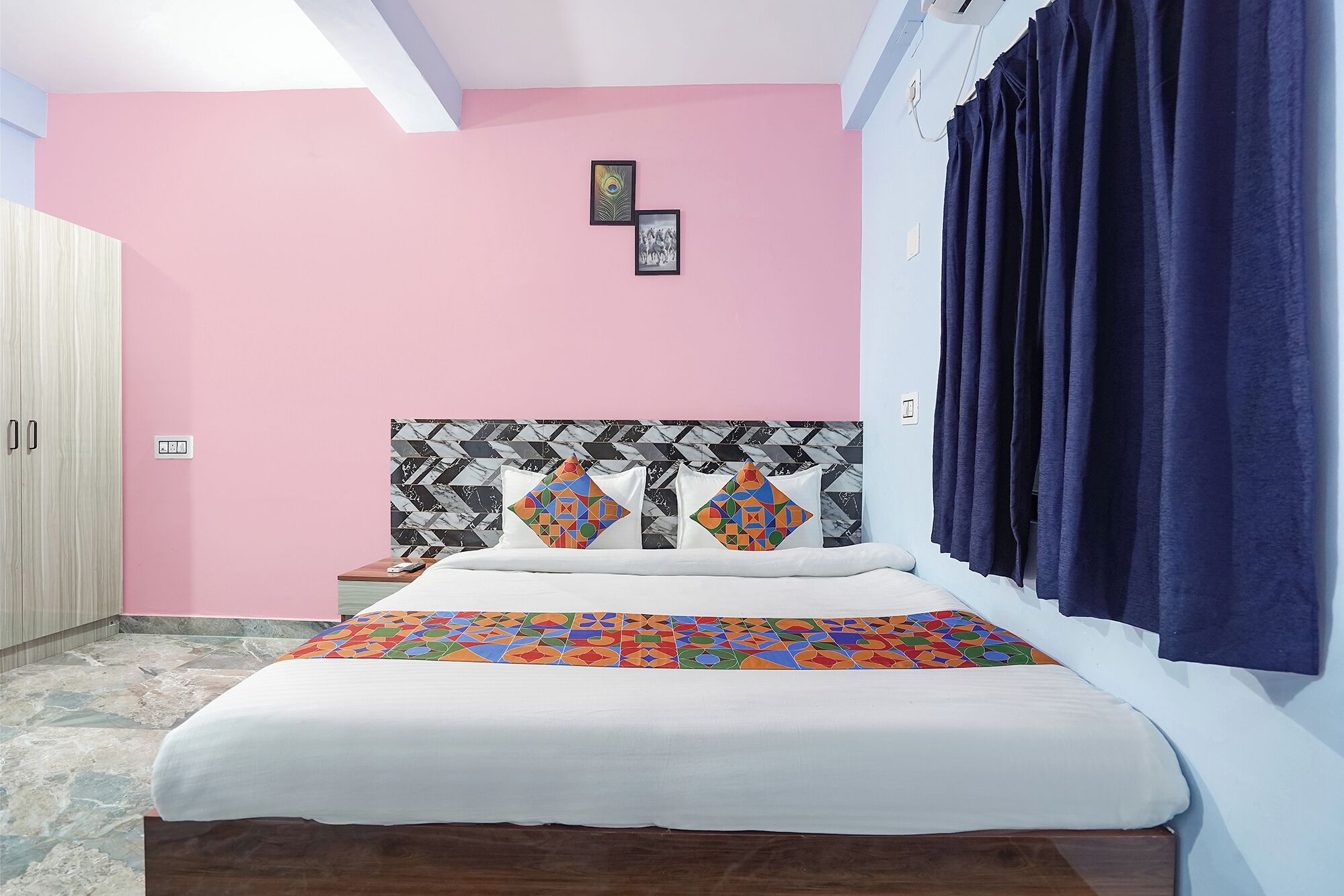 A bedroom with a bed, a headboard with geometric patterns, a pink wall, and a window with dark curtains.
