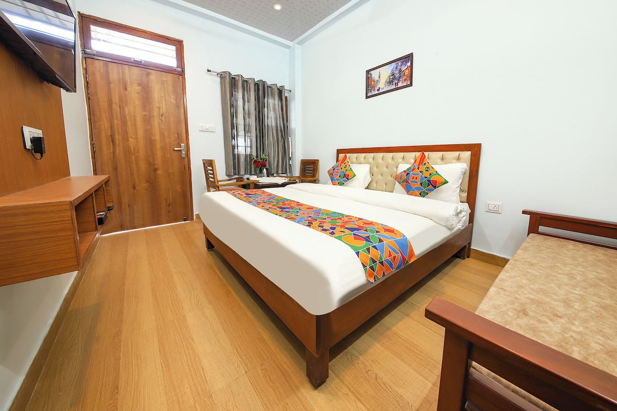 A hotel room with a wooden bed, a desk, a chair, a wardrobe, and a painting on the wall.