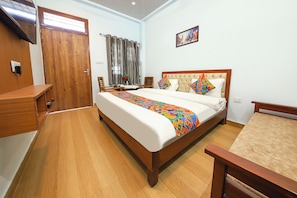 A hotel room with a wooden bed, a desk, a chair, a wardrobe, and a painting on the wall. - Fabhotel Royal Om River Resort (Dehradun)