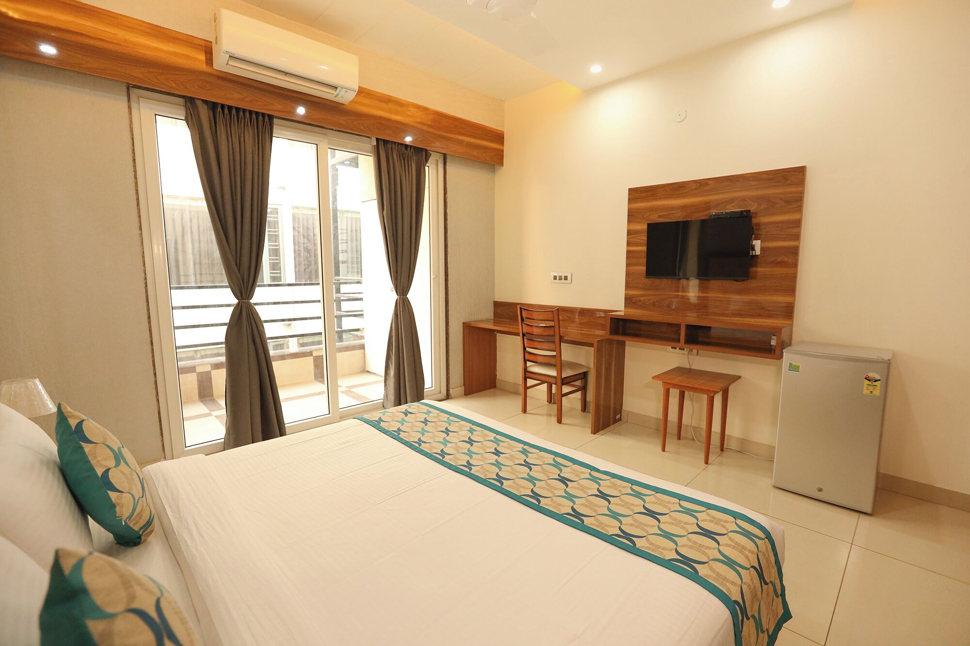 A hotel room with a bed, a desk, a chair, a TV, and a refrigerator.