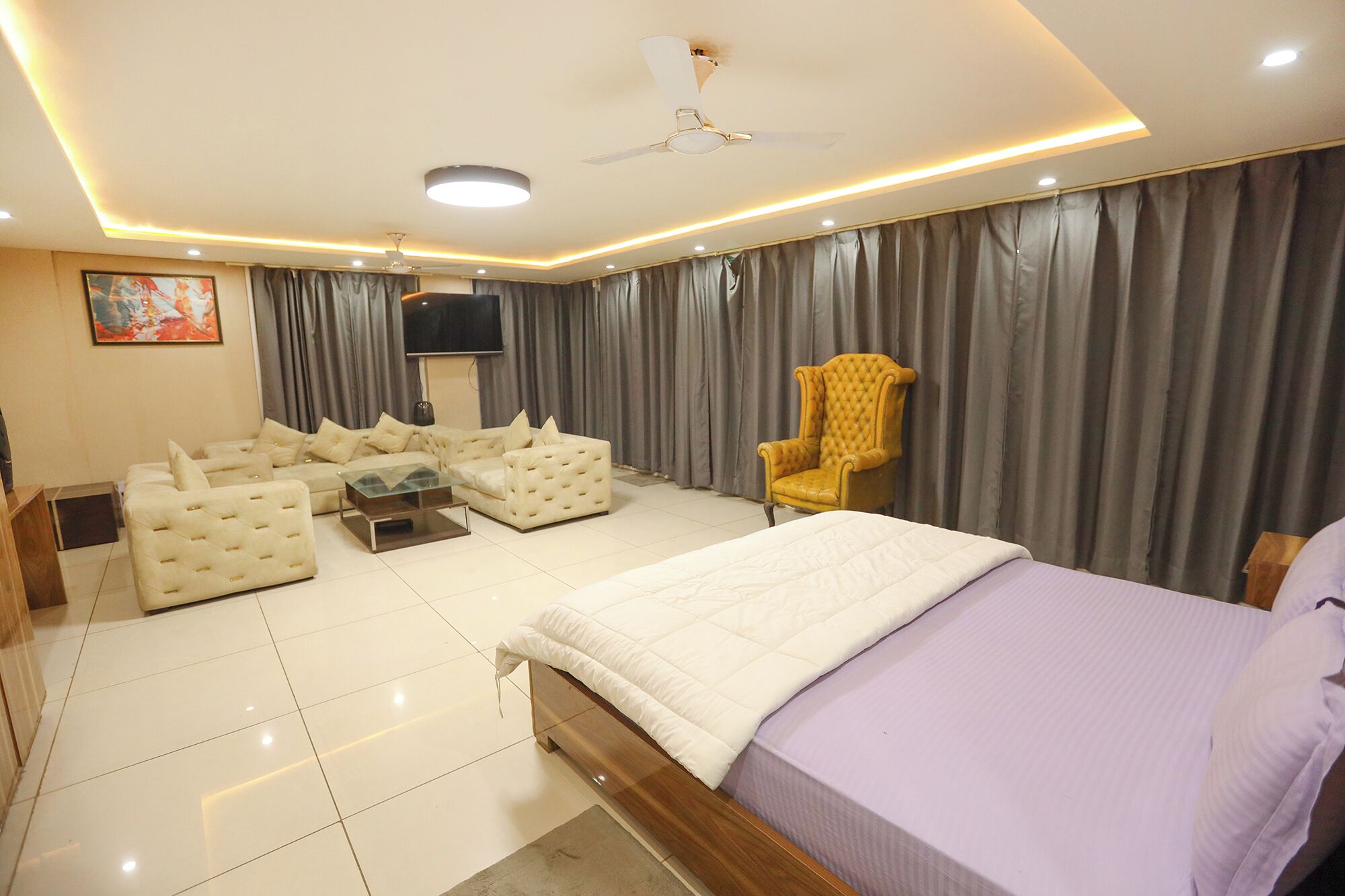 Camera moderna con un letto grande, una poltrona, una sedia, una TV e un ventilatore a soffitto.