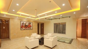 A spacious lobby with a marble floor, white sofas arranged in a semi-circle, a large abstract painting on the wall, and a glass partition with a view. - Fabhotel Starex Inn (Gurugram)