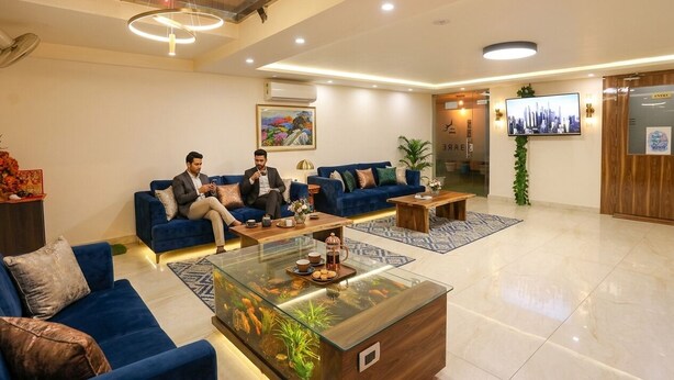 A modern lobby with blue sofas, a glass coffee table, and a TV on the wall. - Fabhotel Starex Inn (Gurugram)