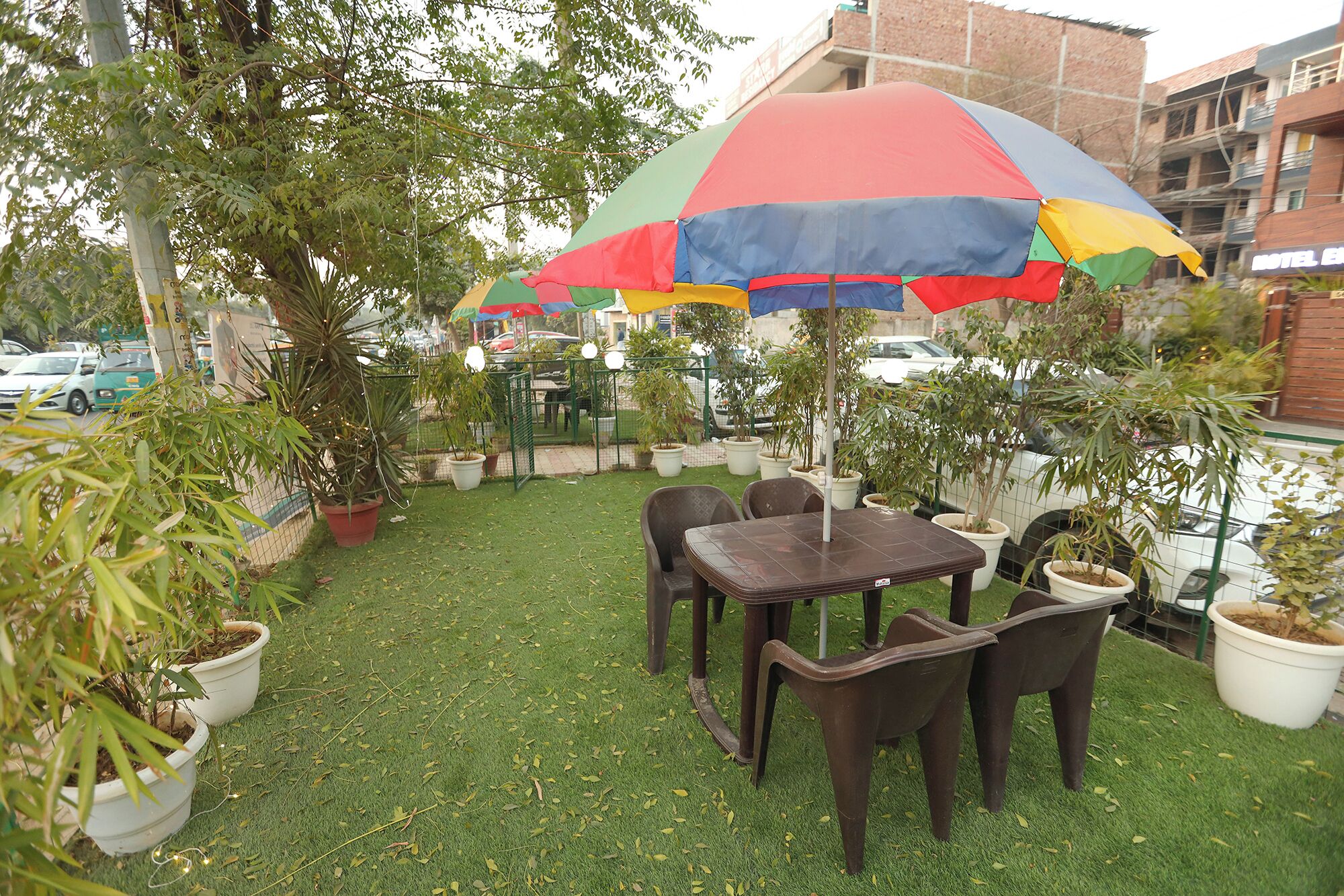An outdoor seating area with a table and chairs under a colorful umbrella, surrounded by potted plants.