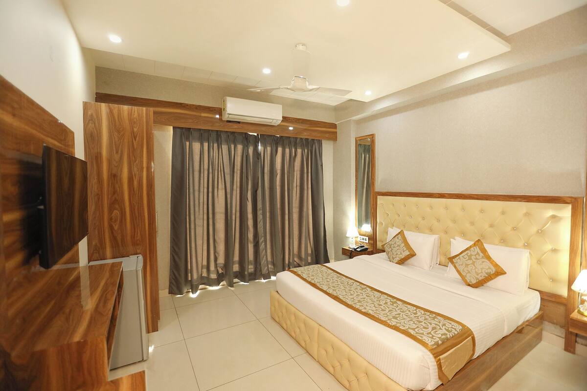 Une chambre d’hôtel avec un grand lit, un téléviseur à écran plat fixé au mur, un ventilateur de plafond et une fenêtre avec des rideaux.