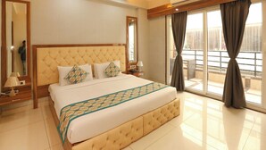 A hotel room with a large bed, a mirror, a bedside table with a lamp, and a view of the outside through large windows. - Fabhotel Starex Inn (Gurugram)
