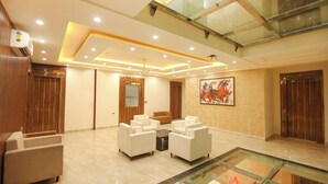 A modern lobby with a glass ceiling, a fireplace, and a seating area with white sofas. - Fabhotel Starex Inn (Gurugram)