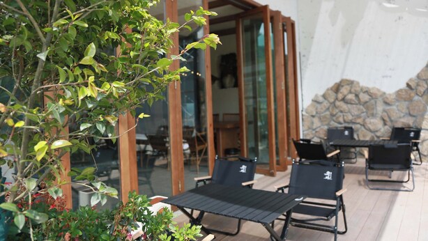 An outdoor patio with a stone wall, a glass door entrance, and black lounge chairs. - Old River Story Long'an Inn (Mianyang)