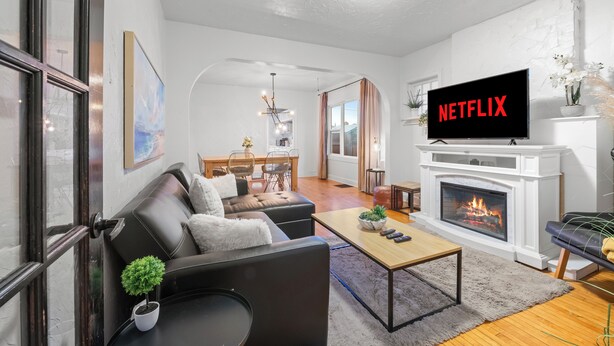 Un salon moderne avec une cheminée, un téléviseur diffusant du contenu de « NETFLIX », et un coin repas à l’arrière-plan.