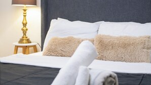 Un lit bien fait, avec des draps blancs, un oreiller beige moelleux et une serviette blanche roulée posée sur le côté.