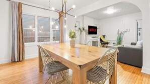 Un salon moderne avec une table à manger en bois, des chaises en osier, un canapé et un téléviseur à écran plat affichant le logo « NETFLIX ».