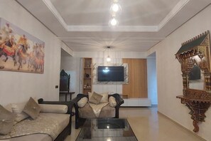 A living room with a sofa, a coffee table, a TV mounted on the wall, and a decorative mirror. - Spacious 120 m² apartment - Downtown | IPTV - Wi-Fi - Netflix (Kenitra)