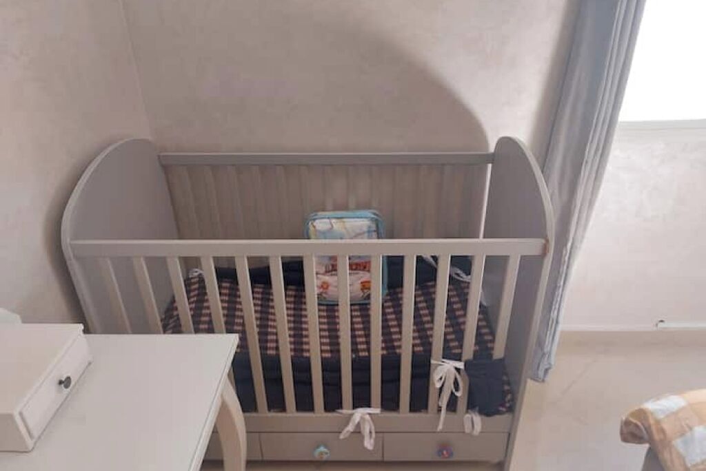A crib with a checkered blanket and a small storage box.