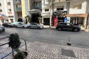 A street view with parked cars, a fruit and vegetable shop, and a building with a sign that reads "Souhail Gsa". - Spacious 120 m² apartment - Downtown | IPTV - Wi-Fi - Netflix (Kenitra)