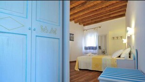 A bedroom with a wooden ceiling, a bed with a yellow and white bedspread, a bedside table with a lamp, and a white wardrobe with decorative elements.