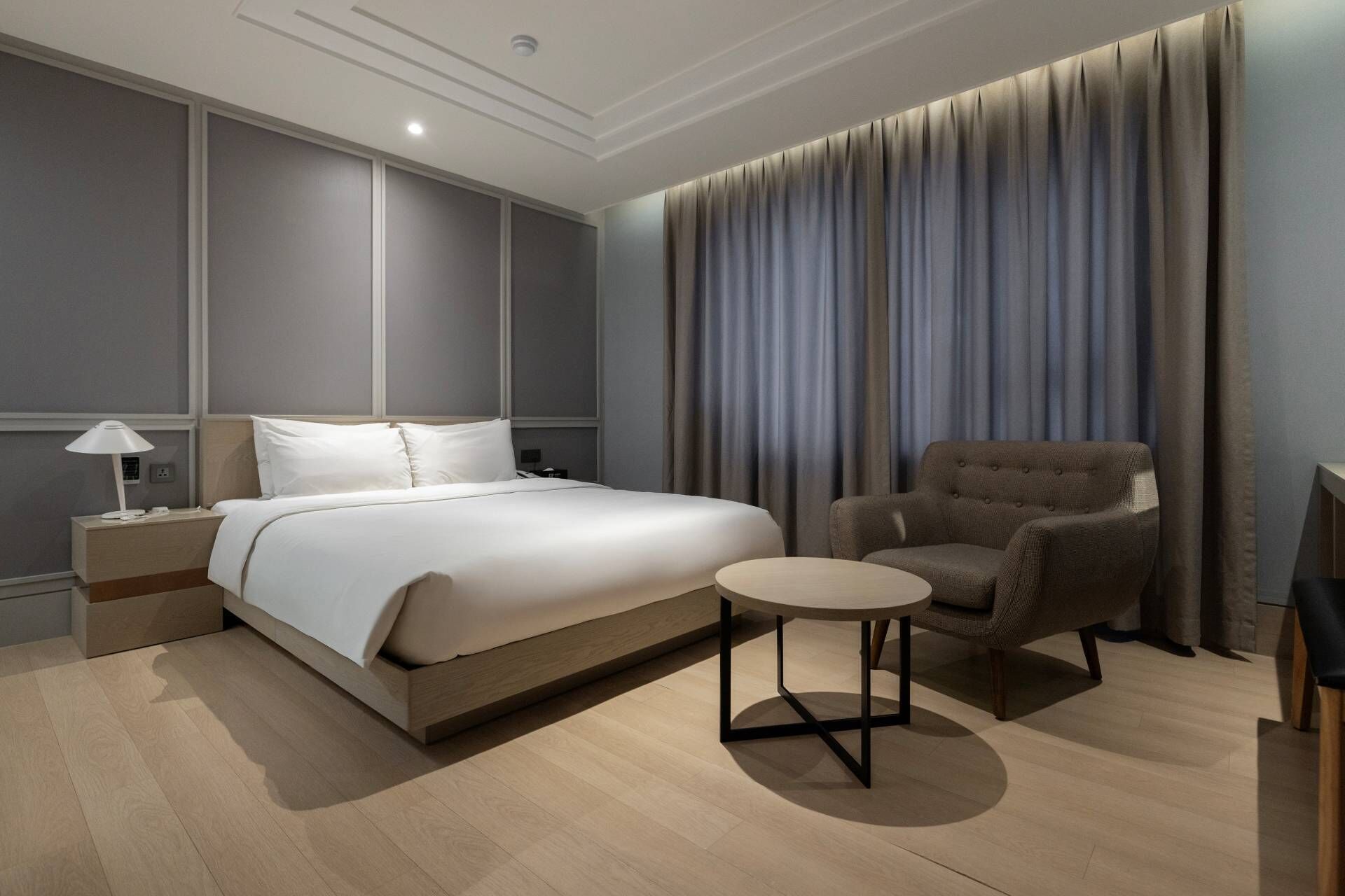 Une chambre d’hôtel moderne avec un grand lit, une petite table ronde, une chaise et un téléviseur.